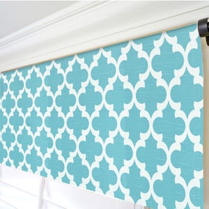 May include: A turquoise and white patterned valance. The fabric features a repeating quatrefoil design. The valance is mounted above a window with white blinds. The color scheme is bright and modern, suitable for various interior styles.