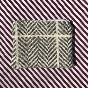 May include: A white and gray chevron patterned zippered pouch. The pouch is lying on a striped burgundy and white surface.