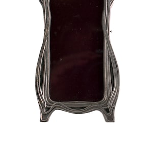 May include: A silver-colored, ornate picture frame with a dark red velvet interior. The frame has a unique, flowing design.