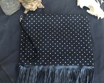 May include: Black clutch bag with a gold polka dot pattern and a black fringe trim. The bag has a black strap.