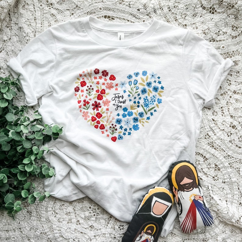 May include: White t-shirt with a floral heart design and the text "Jesus I trust in you".