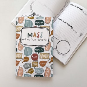 May include: A "Mass Reflection Journal" with a colorful cover featuring speech bubbles with the word "Amen". The journal is open, revealing lined pages for reflections. A rosary is visible in the background.