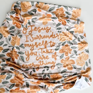 May include: A soft, pink and white throw blanket with a floral pattern and the text "Oh Jesus, I surrender myself to you. Take care of everything".
