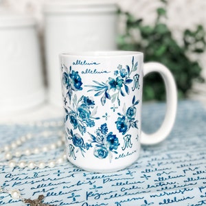 May include: White ceramic mug with a blue and white floral pattern and the word "alleluia" written on it.