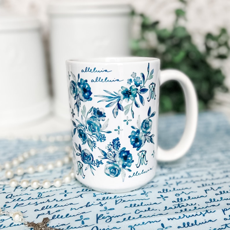 May include: White ceramic mug with a blue and white floral pattern and the word "alleluia" written on it.