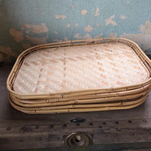 May include: A stack of three rectangular trays crafted from light tan natural rattan. Each tray features a woven base with a tight, repeating geometric pattern and a sturdy, rounded frame made from thicker, smooth bamboo-like stalks.