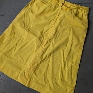 May include: A bright yellow skirt with a straight cut and a drawstring waist. The skirt has two pockets on the sides.