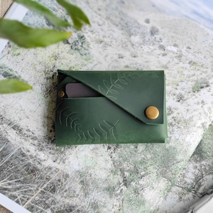 Cartera de piel verde con estampado botánico.
