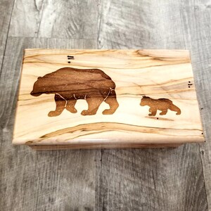 May include: A wooden box with a light brown stain. The box has a bear and a cub etched into the top. The bear and cub are facing the right side of the box.