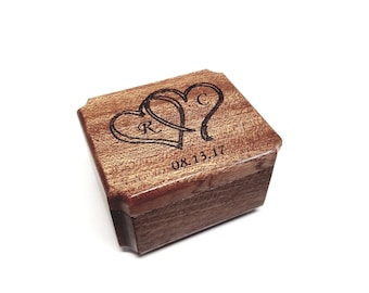 May include: A wooden ring box with two intertwined hearts engraved on the lid. The hearts have the initials "R" and "C" inside. The date "08.13.17" is also engraved on the lid.