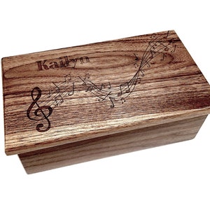May include: A wooden music box with a personalised name "Kailyn" engraved on the lid. The lid features a design of musical notes and a treble clef.