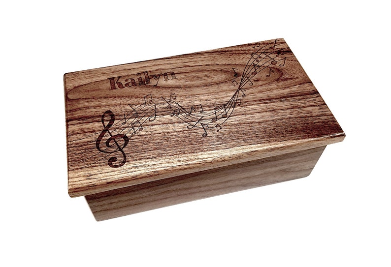 May include: A wooden music box with a personalised name "Kailyn" engraved on the lid. The lid features a design of musical notes and a treble clef.