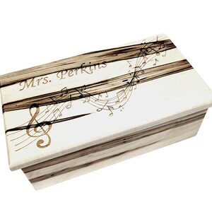 May include: A wooden box with a white lid featuring a treble clef and musical notes design. The lid is personalised with the name "Mrs. Perkins".