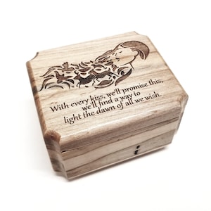 May include: A wooden music box with a carved design of a woman and flowers. The box has a quote engraved on it: "With every kiss, we'll promise this, we'll find a way to light the dawn of all we wish."