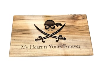 Puede incluir: Una tabla de cortar de madera con un diseño de calavera de pirata y huesos cruzados y el texto "My Heart is Yours Forever" grabado en ella.