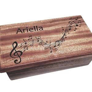 May include: A wooden music box with a personalised inscription "Ariella" and a design of musical notes and a treble clef.