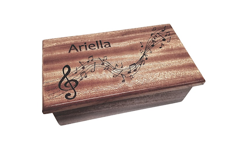 May include: A wooden music box with a personalised inscription "Ariella" and a design of musical notes and a treble clef.