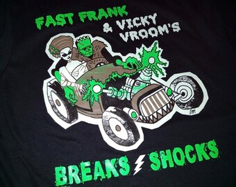 Peut inclure: T-shirt noir avec un graphique vert et blanc d'un couple de monstres conduisant un hot rod avec le texte "Fast Frank & Vicky Vroom's Breaks Shocks".