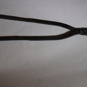 May include: A pair of black metal pliers with a unique design. The pliers have a curved handle and a pair of jaws with a rounded opening.