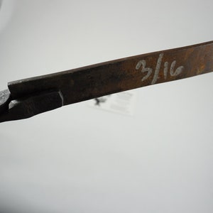 May include: Close-up of a rusty metal tool with a handle and a blade. The blade is marked with the fraction "3/16".