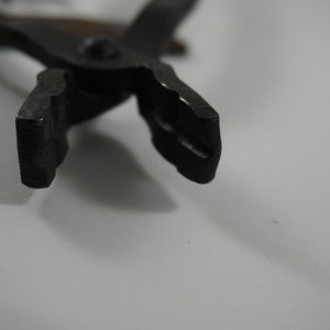 May include: Close-up of the jaws of a pair of black metal pliers. The jaws are open and the tips are sharp.