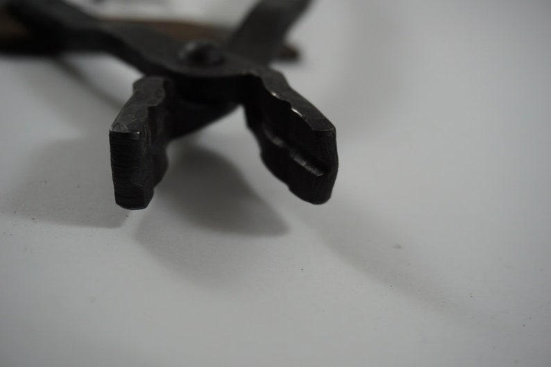 May include: Close-up of the jaws of a pair of black metal pliers. The jaws are open and the tips are sharp.