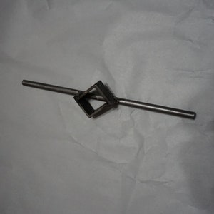 May include: A metal tool with a square-shaped hole in the center and a long handle. The tool is designed for tightening or loosening square-shaped nuts.