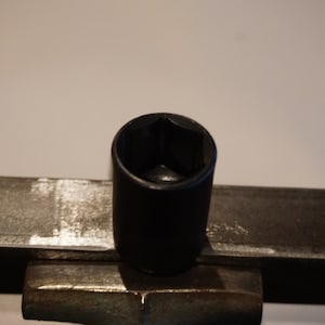 Op de afbeelding: Een zwarte steeksleutel met een zeskantige opening, liggend op een metalen oppervlak.