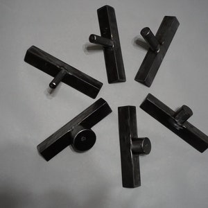 May include: Six black metal hooks with a rounded top, mounted on a wall. The hooks are arranged in a starburst pattern.