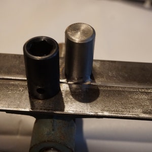 Op de afbeelding: Een zwarte steeksleutel en een zilveren metalen staaf zijn vastgeklemd in een metalen bankschroef. De bankschroef is gemarkeerd met "SWISS".