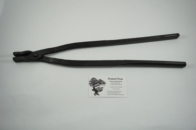 May include: Black metal blacksmith tongs with a rounded handle. The tongs are approximately 18 inches long.