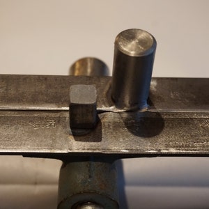 May include: Close-up of a metal tool with two flat pieces of metal and a round metal rod. The metal pieces are attached to the rod with a weld. The tool is likely used for bending or shaping metal.