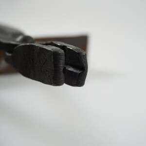 May include: Close-up of the jaws of a black metal pliers. The jaws are open and have a slight curve to them.