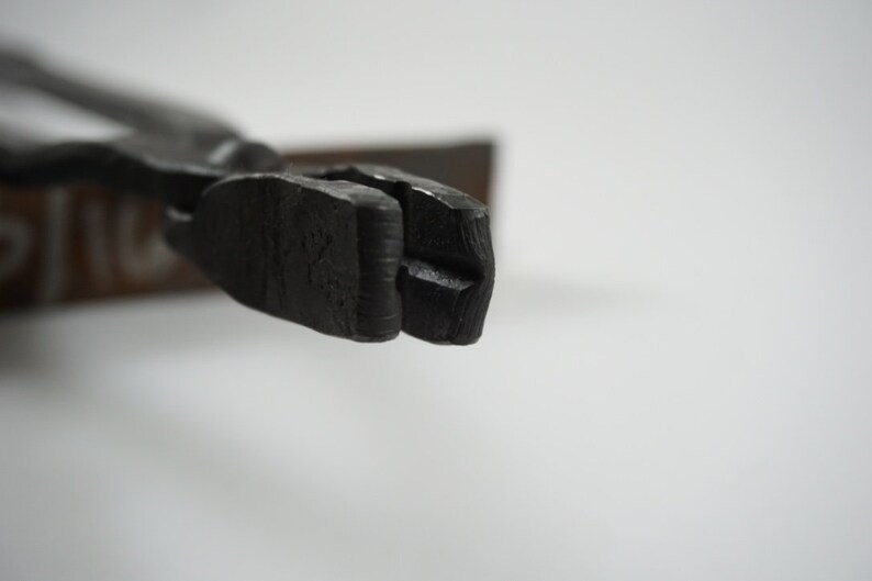 May include: Close-up of the jaws of a black metal pliers. The jaws are open and have a slight curve to them.