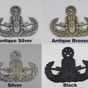 May include: Four metal badges in antique silver, antique bronze, silver, and black. Each badge features a central design with a star, lightning bolts, and a bomb shape, surrounded by a laurel wreath and a star at the top. The text "Antique Silver", "Antique Bronze", "Silver", and "Black" are below each badge.