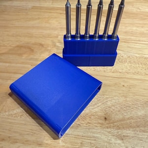 May include: A set of six silver soldering iron tips in a blue holder, with a matching blue cover. The tips are various shapes and sizes. The holder and cover are made of plastic. The items are on a wooden surface.