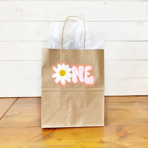 May include: A brown paper gift bag with a white daisy and the word "ONE" in pink letters.