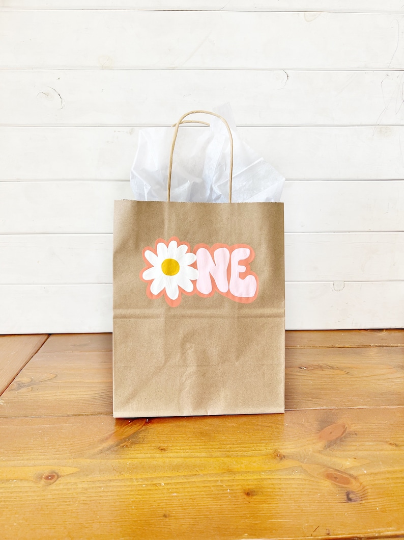May include: A brown paper gift bag with a white daisy and the word "ONE" in pink letters.