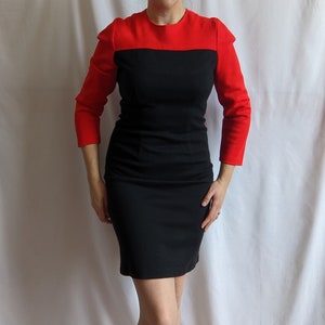 Peut inclure: Une robe noire et rouge avec une silhouette ajustée et des manches trois-quarts. La robe a un haut rouge et un bas noir.