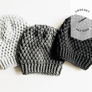 Może przedstawiać: Trzy czapki wykonane na szydełku w różnych odcieniach szarości. Czapki są wykonane z fakturowanym ściegiem, który tworzy nierówną powierzchnię. Czapki są ułożone w rzędzie, z najjaśniejszą szarą czapką po lewej stronie, najciemniejszą szarą czapką po prawej stronie i średnio szarą czapką pośrodku. Tekst "CROCHET PATTERN" jest widoczny w prawym górnym rogu obrazu.