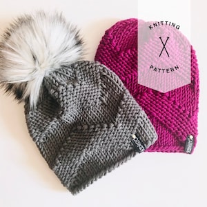 May include: Two knitted hats, one gray with a white pom pom and one pink. Both hats have a textured pattern and a small black tag with the word "kooked" on it. The pink hat has a white label with the words "Knitting Pattern" and a pair of knitting needles.