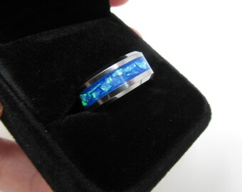 Pode incluir: Um anel de prata com uma incrustação de opala azul e verde. O anel está em uma caixa de anel de veludo preto.