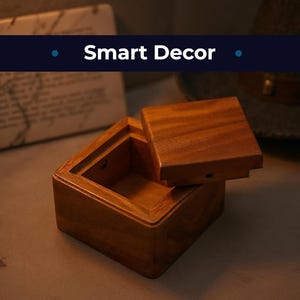 Op de afbeelding: Een vierkante houten doos met een iets geopende deksel, die de houtnerf laat zien. De doos heeft een warme bruine kleur en lijkt handgemaakt. De tekst "Smart Decor" wordt boven de doos weergegeven.