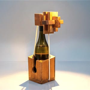 May include: A wooden wine bottle puzzle with a bottle inside. The puzzle is made of interlocking wooden blocks and a hexagonal base. The bottle is green glass, and the puzzle is held together with white rope.