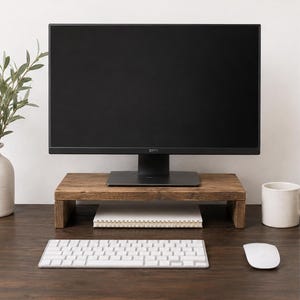 May include: A rectangular wooden monitor stand with a dark brown finish, featuring a flat top surface and two side supports. The stand is positioned on a dark wooden desk, holding a black Dell computer monitor, with a white keyboard and mouse.