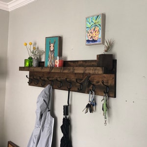 May include: A dark brown wooden shelf with metal hooks, a white shelf, and a llama print on the wall. There are keys, a green plant, and a candle on the shelf.