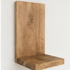 May include: A wall-mounted L-shaped shelf crafted from light brown wood with a visible natural grain pattern. The shelf features a tall vertical back panel and a horizontal base platform, providing a simple structure for display or storage.