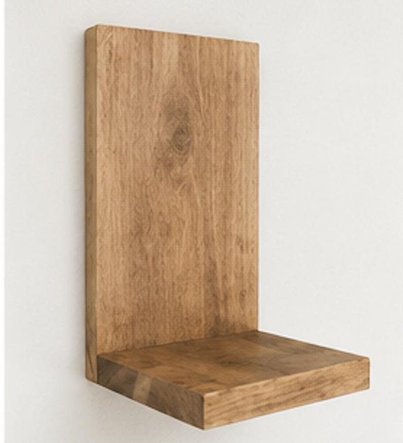 May include: A wall-mounted L-shaped shelf crafted from light brown wood with a visible natural grain pattern. The shelf features a tall vertical back panel and a horizontal base platform, providing a simple structure for display or storage.
