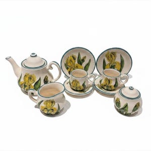 Könnte beinhalten: Ein Keramik-Teeservice mit Teekanne, Sahnekännchen, Zuckerdose, zwei Tassen und zwei Untertassen. Das Set ist mit gelben Irisblüten und grünen Blättern mit blauem Rand bemalt.