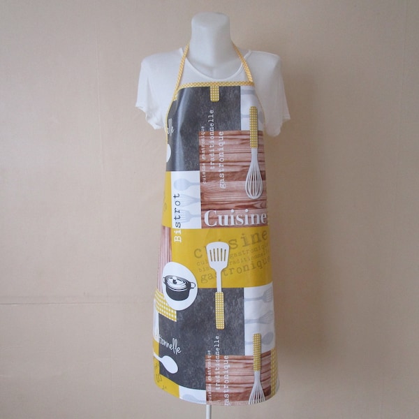 Tablier femme en toile cirée jaune, grise et blanche avec des motifs de cuisine